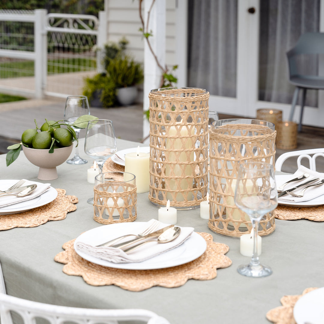 Outdoor table setting with candles, glasses, and plates on a patio.