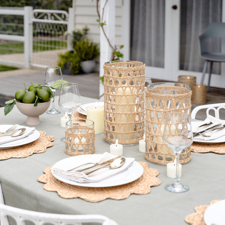 Outdoor table setting with candles, glasses, and plates on a patio.