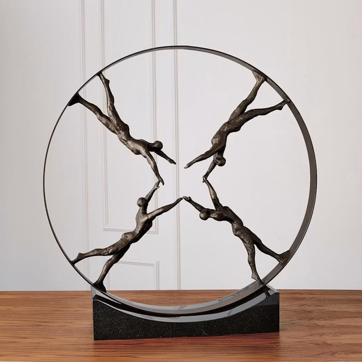 Bronze sculpture of four abstract figures in a circular arrangement on a wooden surface.